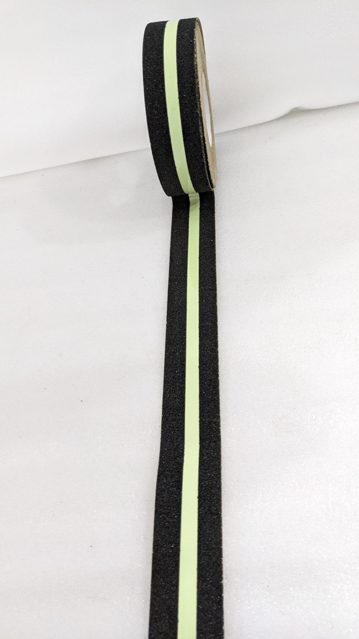 Dolphy glow stripe anti-skid tape unrolled, showing the gritty black edges and luminous centre