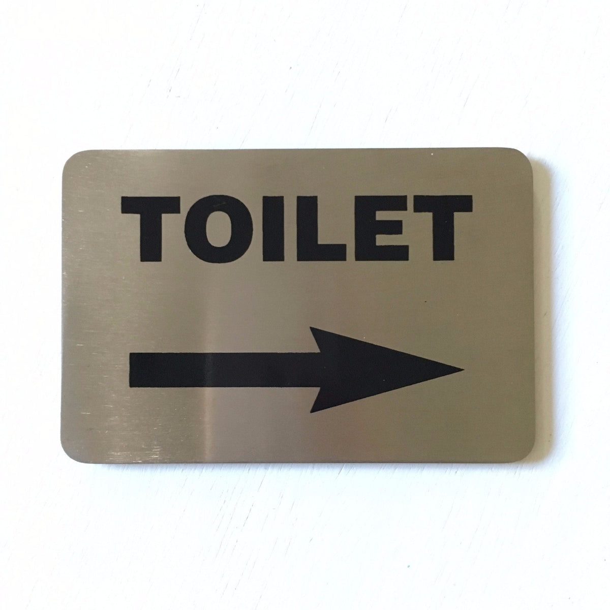 Stainless steel TOILET sign with an arrow pointing right