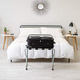 Dolphy stainless steel folding luggage rack holding a suitcase at the foot of a hotel bed