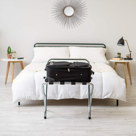 Dolphy stainless steel folding luggage rack holding a suitcase at the foot of a hotel bed