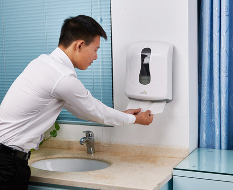 Man taking a paper towel from a Dolphy dispenser mounted beside a washroom basin