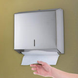 Hand taking a paper towel from the Dolphy stainless steel towel dispenser on a wall