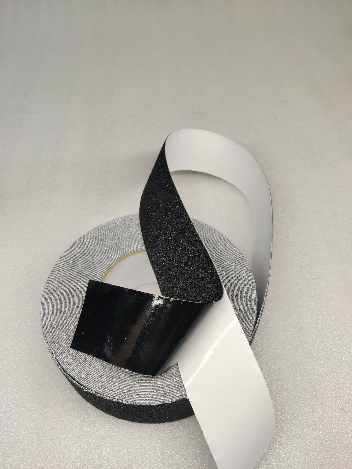 Dolphy black anti-skid tape with the white release liner peeled back from the adhesive