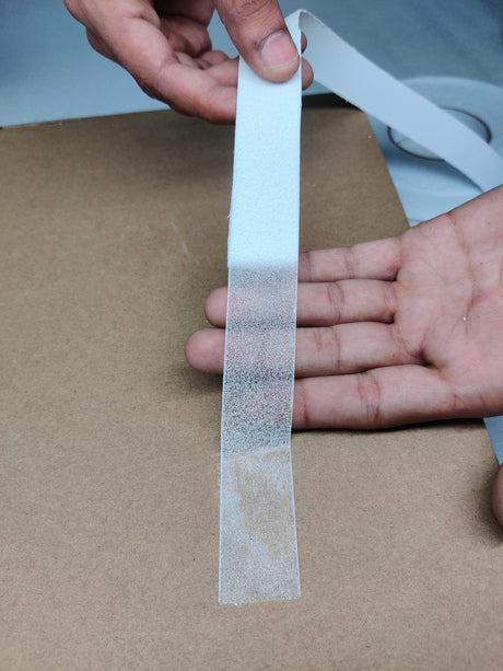 Clear Dolphy anti-slip tape held over a hand, showing its see-through gritty surface